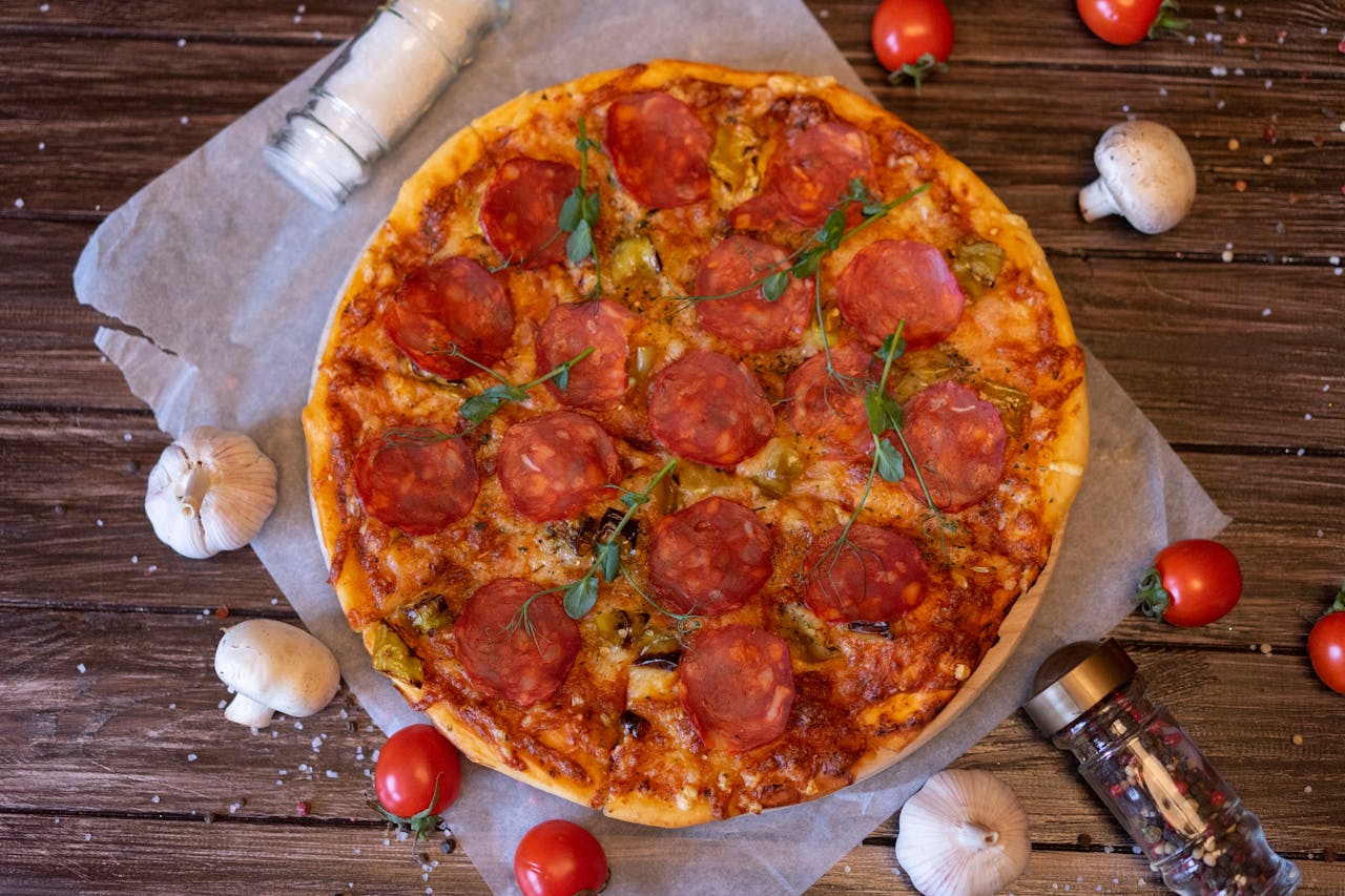 home-hero-2 A mouthwatering pepperoni pizza topped with savory ingredients on a rustic table setting.